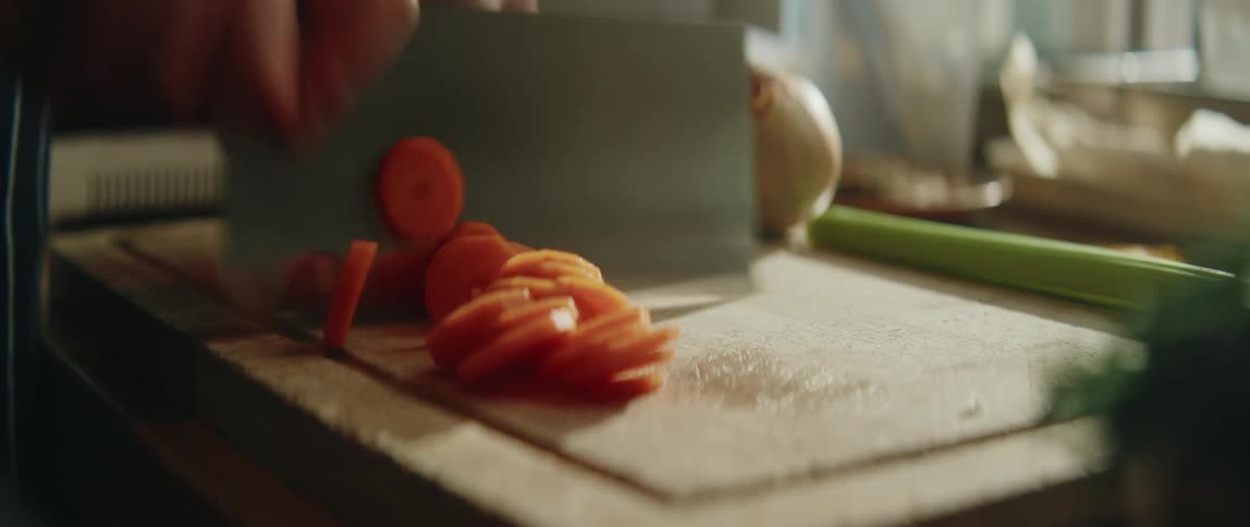 Sliced tomato on a cutting board with a knife in motion and vegetables around