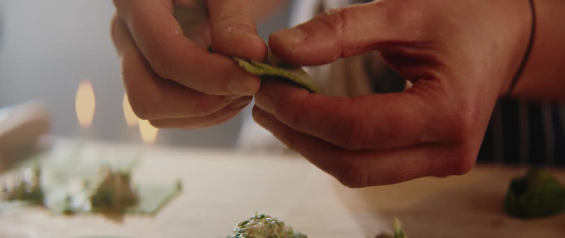 Hands shaping green dough filled with a mixture of ingredients on a work surface
