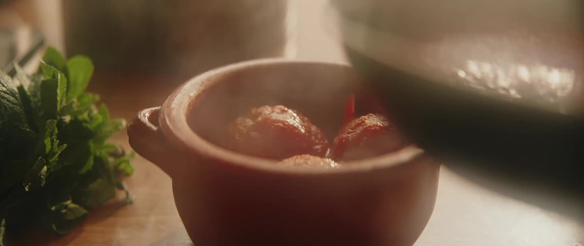 A person serving freshly prepared meatballs from a pan into a bowl