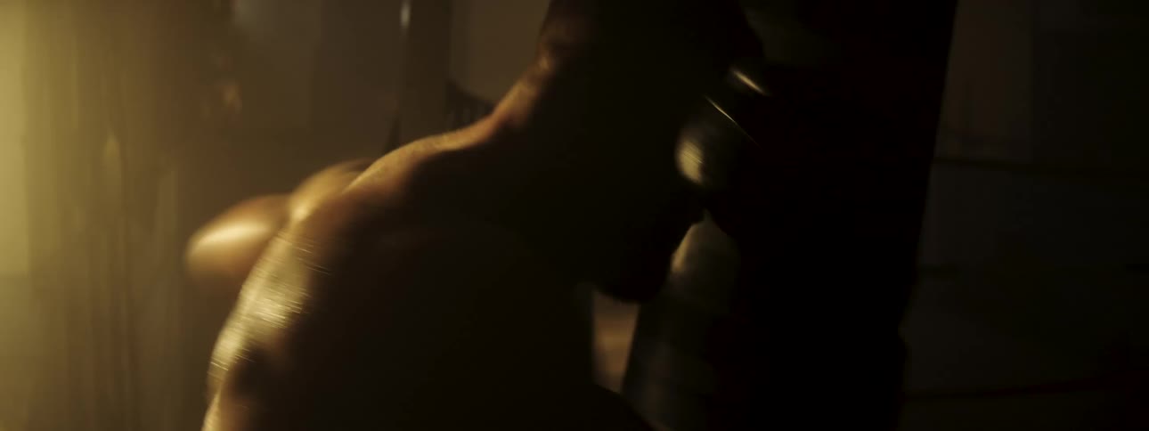 Boxer throwing punches during training under warm lighting with sweat visible on the body