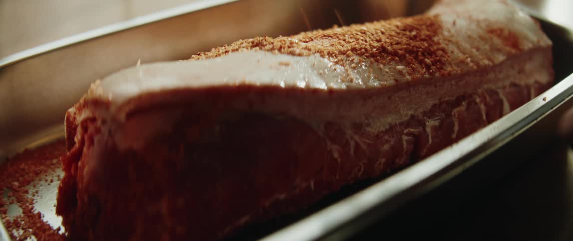 Adult human hands rubbing seasoning on a piece of a meat inside a roasting tin indoors during day time