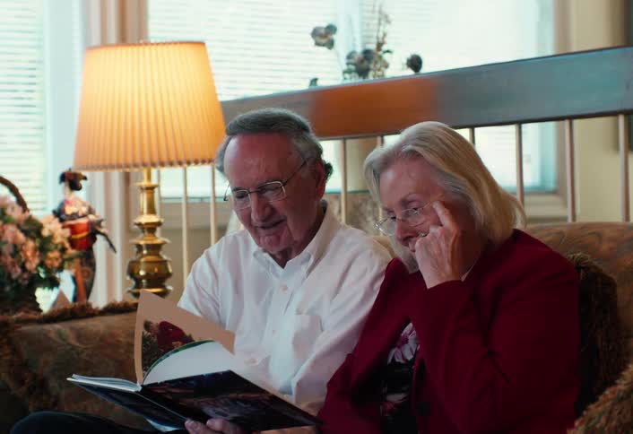 Elderly couple sitting together on the couch looking at a book