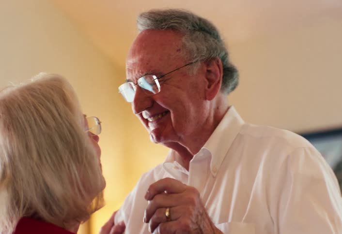 Elderly couple laugh and talk as they dance together in the living room