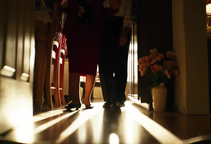 Elderly couple walking together down an indoor hallway lit by natural light coming through a doorway
