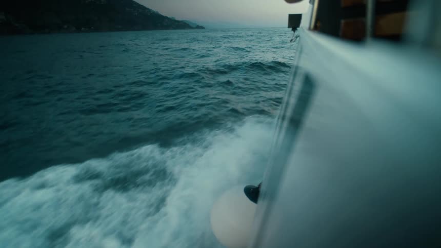 Boat moving across the sea with a foamy water wake alongside the hull and coastline in the background