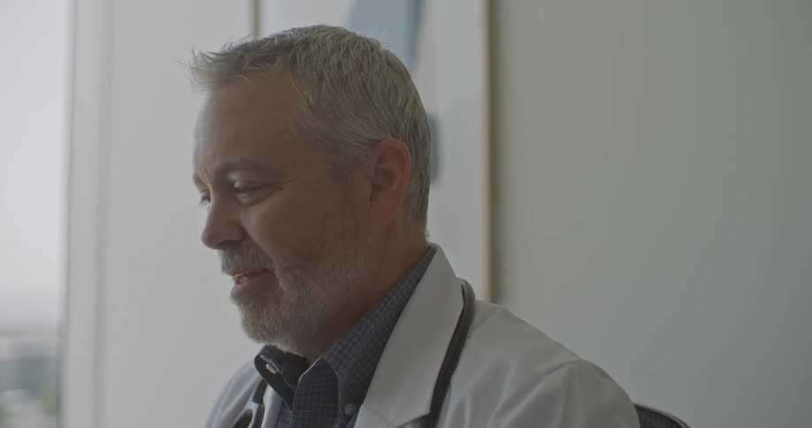 Older male doctor sits in his office speaking during the daytime