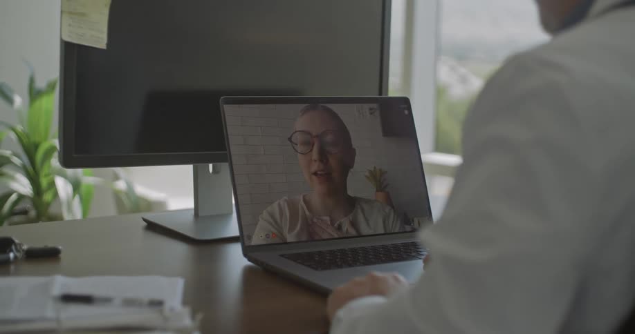 Doctor sitting at his desk having a video conversation with a woman holding her hand on her chest
