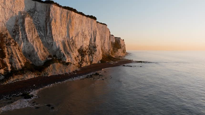 A calm sea with a few ripples hitting the shoreline near a cliff