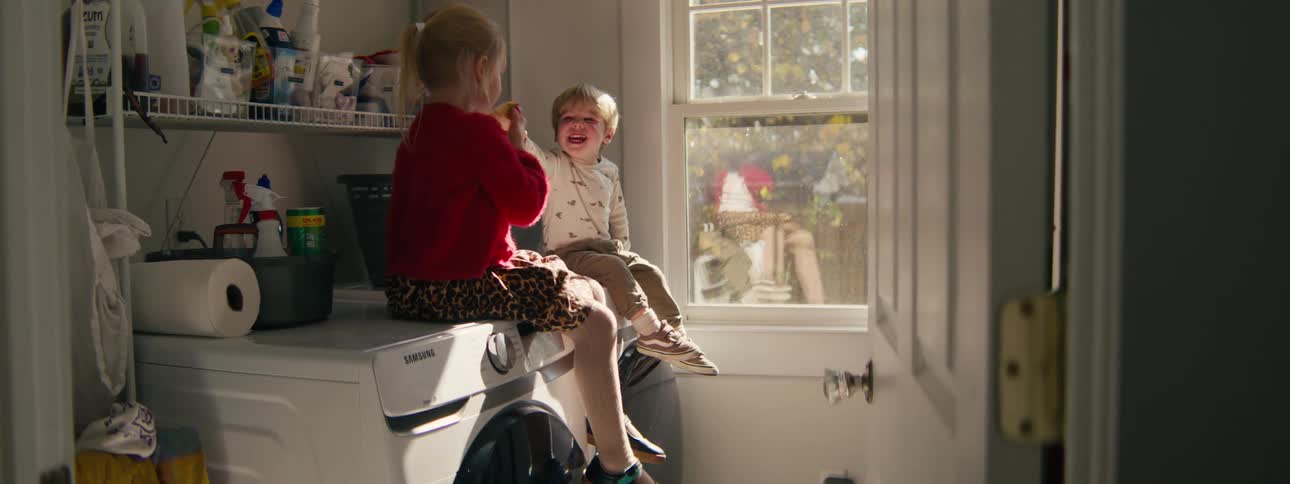 Two kids sitting on a washing machine in a laundry room at midday having fun together