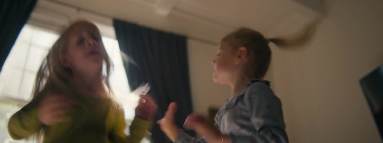 Two kids jumping and playing on a bed inside a bedroom at midday