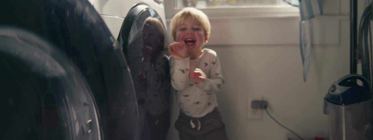 Child indoors smiling beside a household appliance with natural light coming through a window