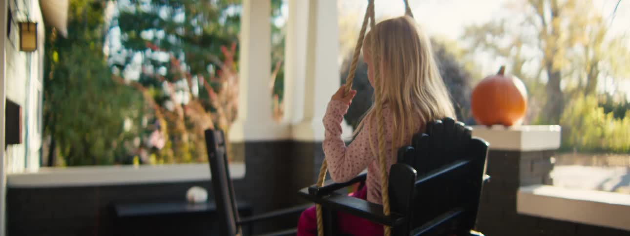 Girl sitting in a swing on the front porch as her little sister spins her around