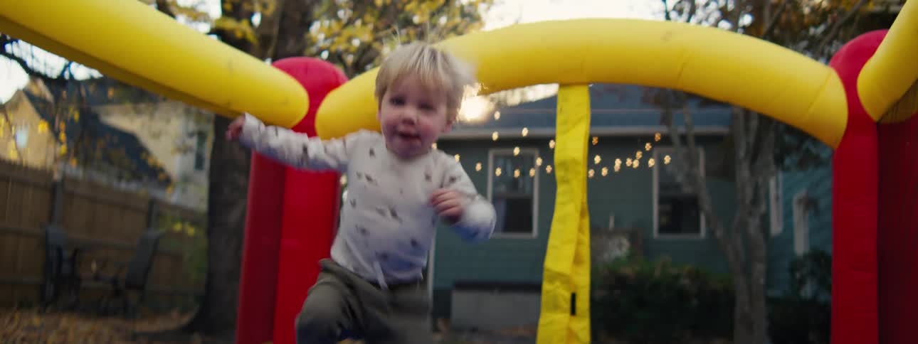 Toddler stands on an inflatable play structure with colorful arches in a residential backyard