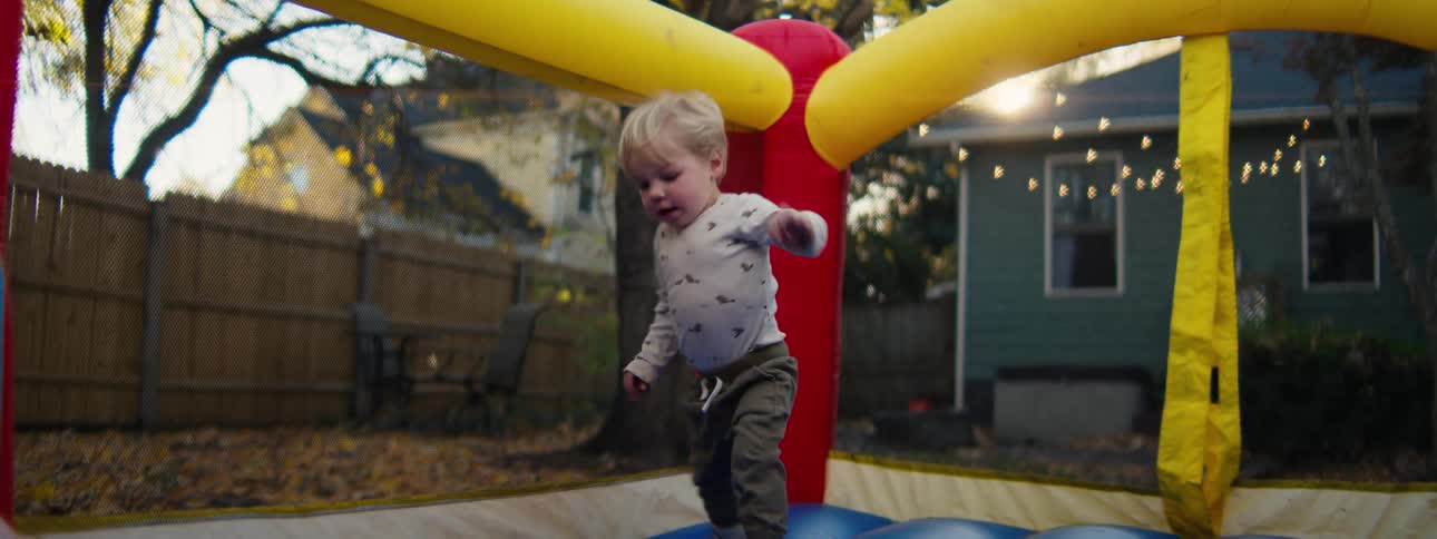 Toddler walks on a colorful inflatable toy in a residential backyard at dusk