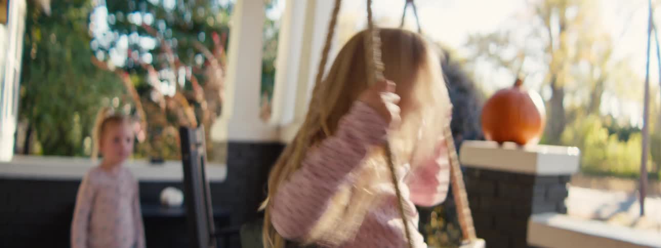 Child playing on a rope swing on an outdoor porch with a decorative pumpkin and greenery in the background