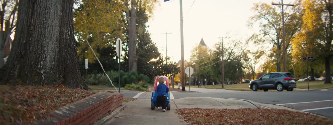 The child pushes a kart on the sidewalk