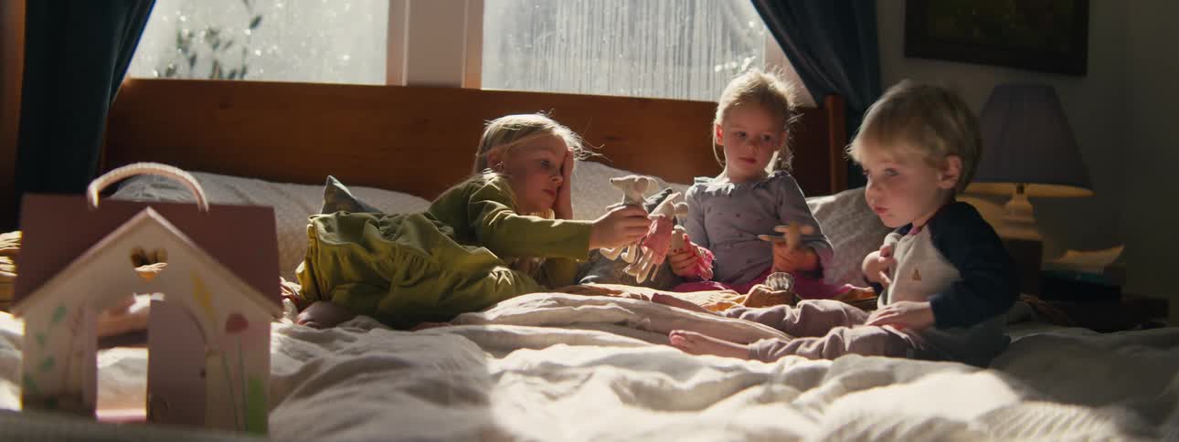 Three young children playing with toys together on a large bed