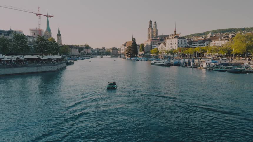Small tour boat cruising down a historic european river lined with gothic cathedrals clock towers and classic architecture under a clear sky
