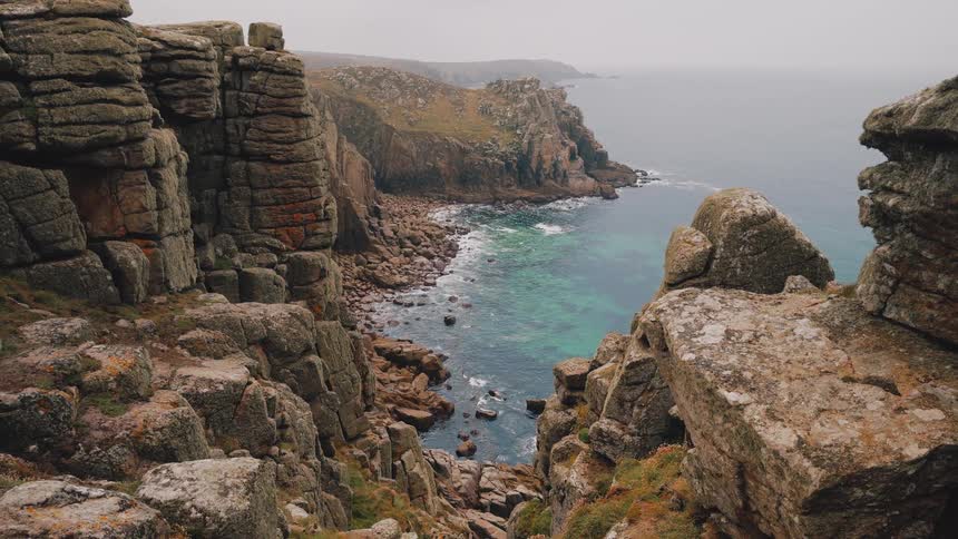 Rocky cliffs forming a coastal cove with turquoiseblue sea and stones along the shoreline