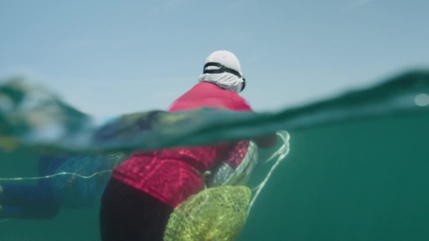 Person wearing a dive mask floats at the ocean surface with equipment partially submerged