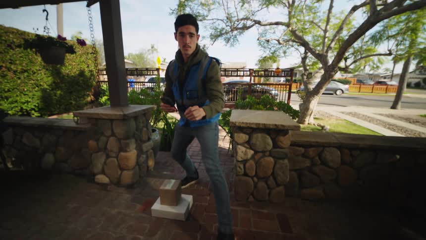 Delivery man leaves packages on the porch and takes a picture with his phone then rings the doorbell and waves as he leaves