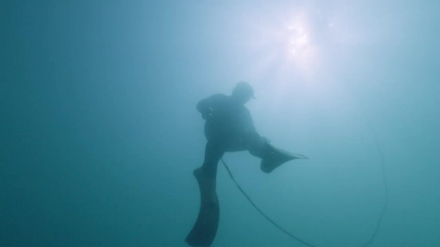 Person submerged performing an underwater activity with breathing equipment and a connected cable in a marine environment
