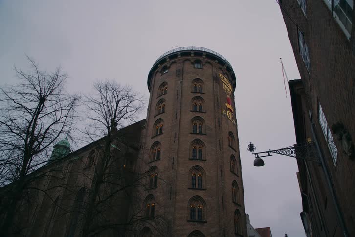 A historic cylindrical tower stands tall above nearby buildings under a cloudy sky