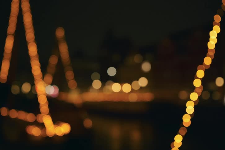 This video features a warm outoffocus night scene decorated with glowing strings of amber lights the soft bokeh effect creates a festive and cozy atmosphere over a dark urban backdrop
