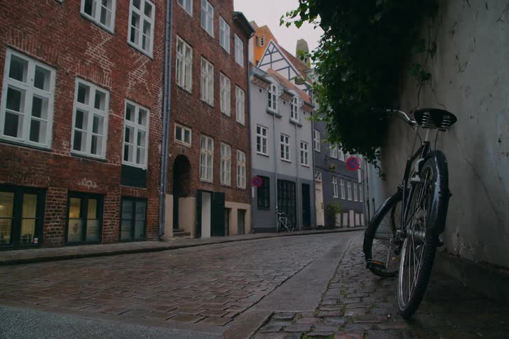 A bicycle resting against a wall on a street lined with residential buildings at midday