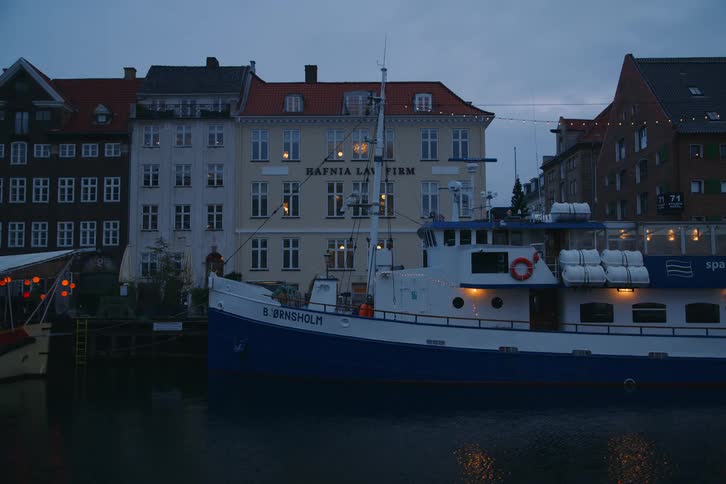 A large ship rests in a canal with historic buildings silhouetted against a dusky sky