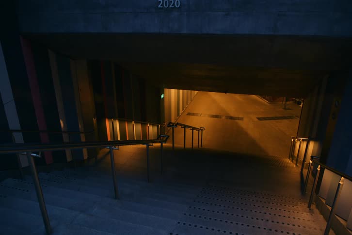 Staircase descends into an underground passage with artificial lighting in an urban night setting