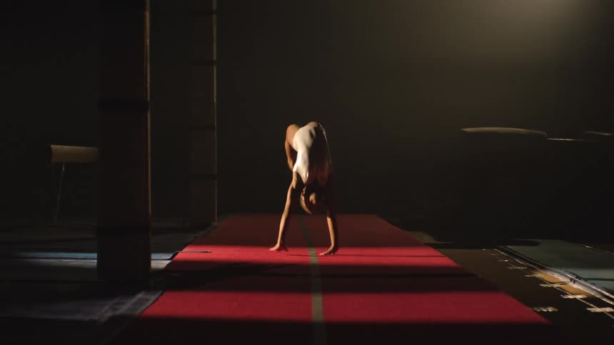 Athlete performs a series of back handsprings on a red mat in a dramatically lit gym