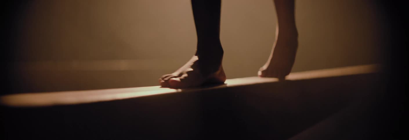 Gymnast walks on the balance beam in a dimly lit area