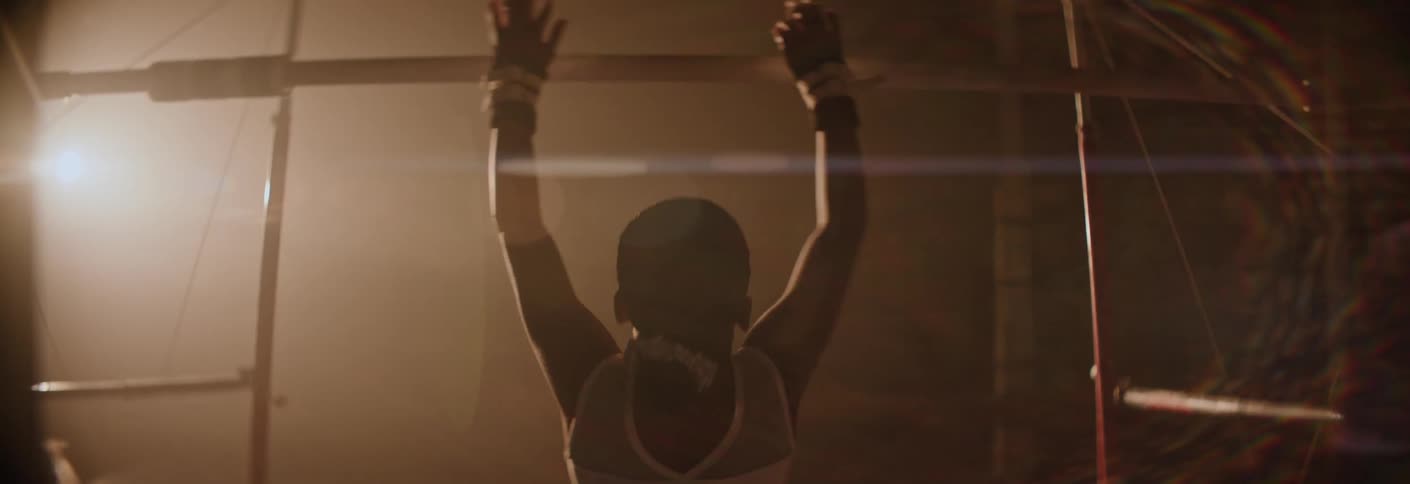 A gymnast in a shimmering silver leotard walks toward the uneven bars in a hazy spotlighted gym to begin her routine