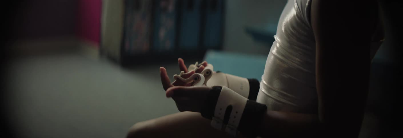 A young gymnast sits in a locker room looking down with a focused and serious expression she is shown adjusting her white gymnastic grips and wristbands preparing for a competition