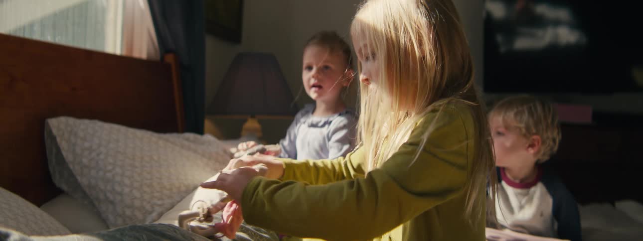 Three young children playing quietly with stuffed toys on a bed in a sunlit bedroom