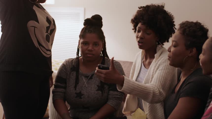 A group of women gather around a smartphone