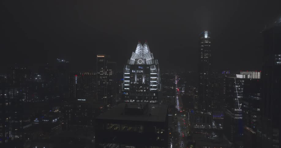 A mesmerizing city skyline rises into the night air its illuminated skyscrapers and the iconic glowing peak of frost bank tower shimmering brightly above the dark busy streets and moving traffic below