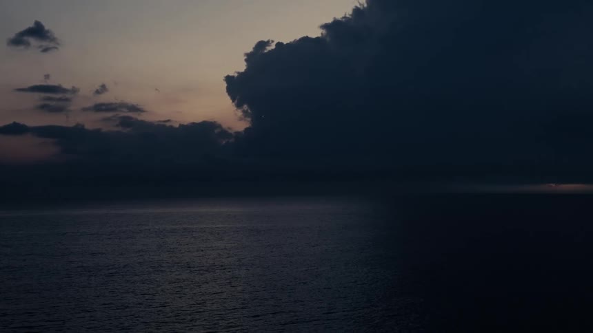 Dark cloud advances over the ocean at dusk with a band of light on the horizon