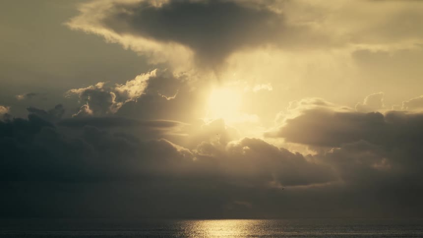 Sun emerges between dense clouds over the ocean with a bright reflection on the water surface