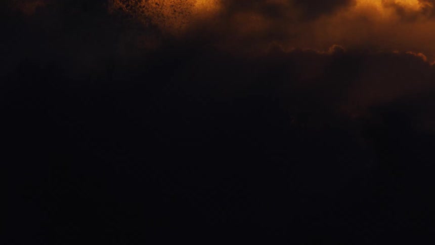 The sun glows among clouds in an orange sky as waves splash rolling in to shore