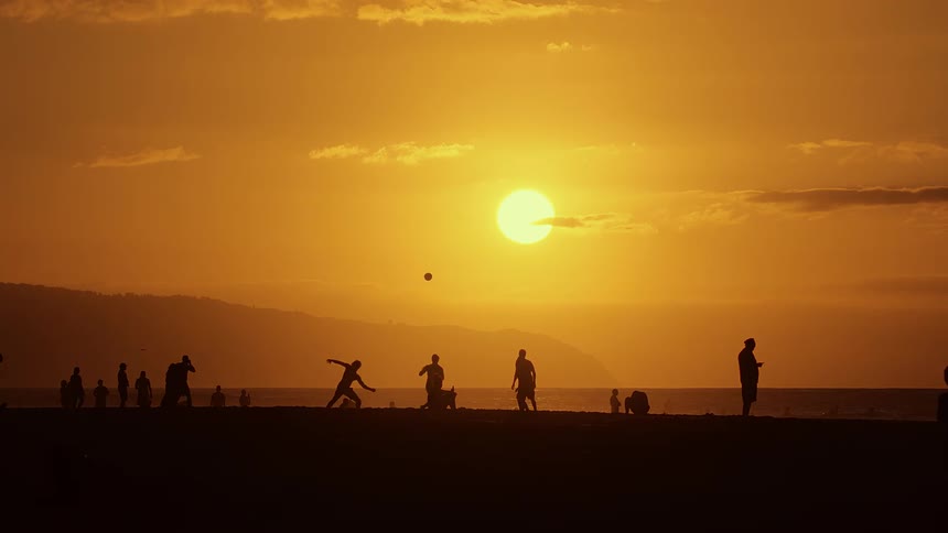 Silhouetted people playing together and having fun on the beach during a sunset