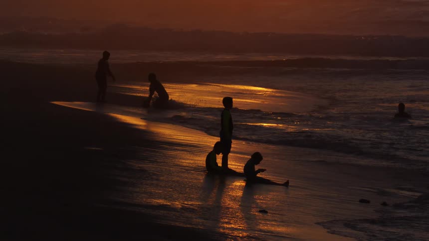 People sitting and standing on the beach as the sun sets