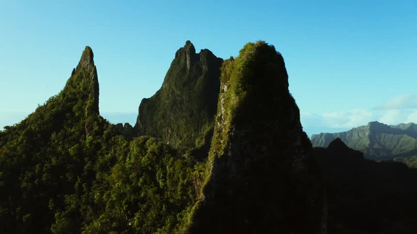 Aerial view of lush green mountains rising from a tropical forest under a clear blue sky