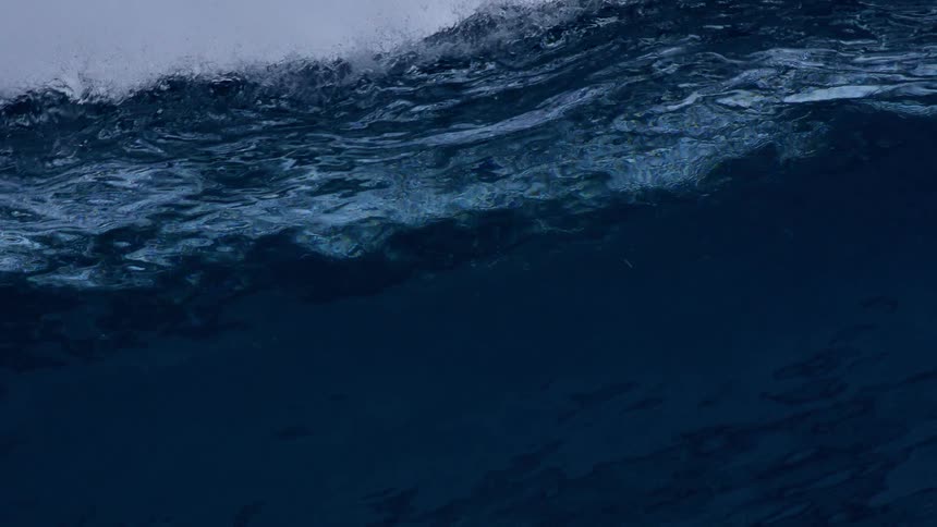 Ocean wave seen from below with a turbulent surface and varying blue tones