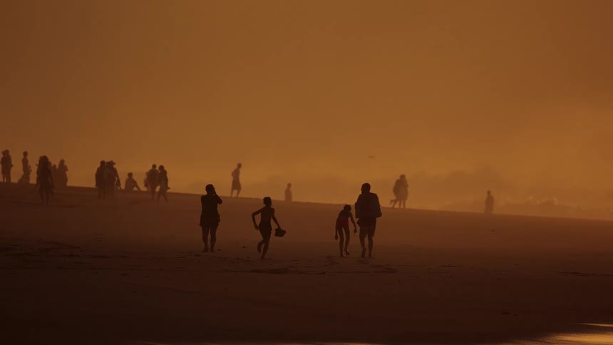 People walk and play on the beach as waves roll in to shore
