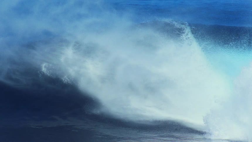 Ocean wave breaking with intense spray and blue variations across the water surface