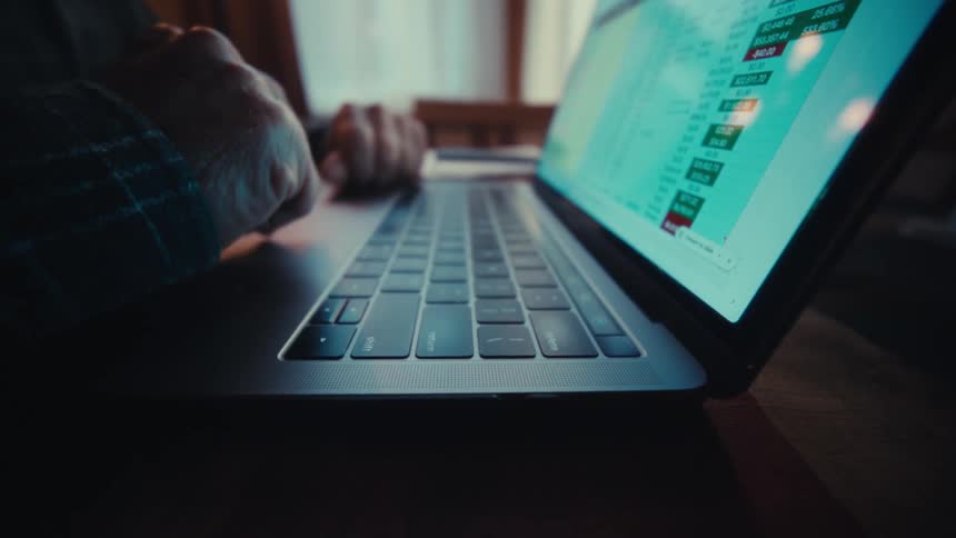 Fingers pressing a laptop keyboard with a spreadsheet open on the screen in an indoor environment