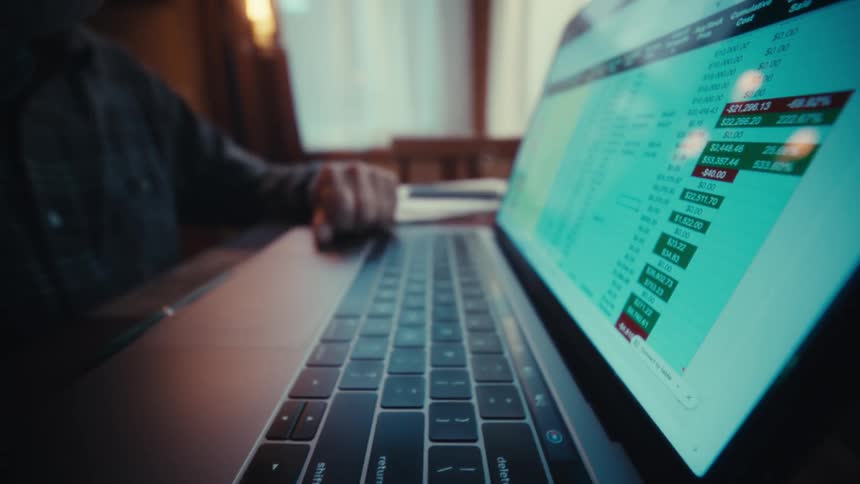 A finger typing on a laptop keyboard with a glowing spreadsheetstyle interface on the screen