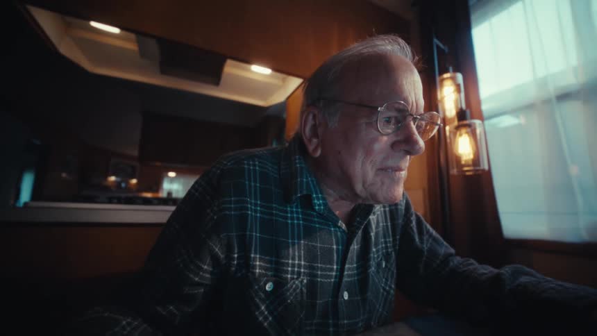 An elderly man in a plaid shirt is shown working at a desk alternating between using a calculator and typing on a laptop the video captures his focused expressions in closeup shots as he adjusts his glasses and looks thoughtfully toward his screen